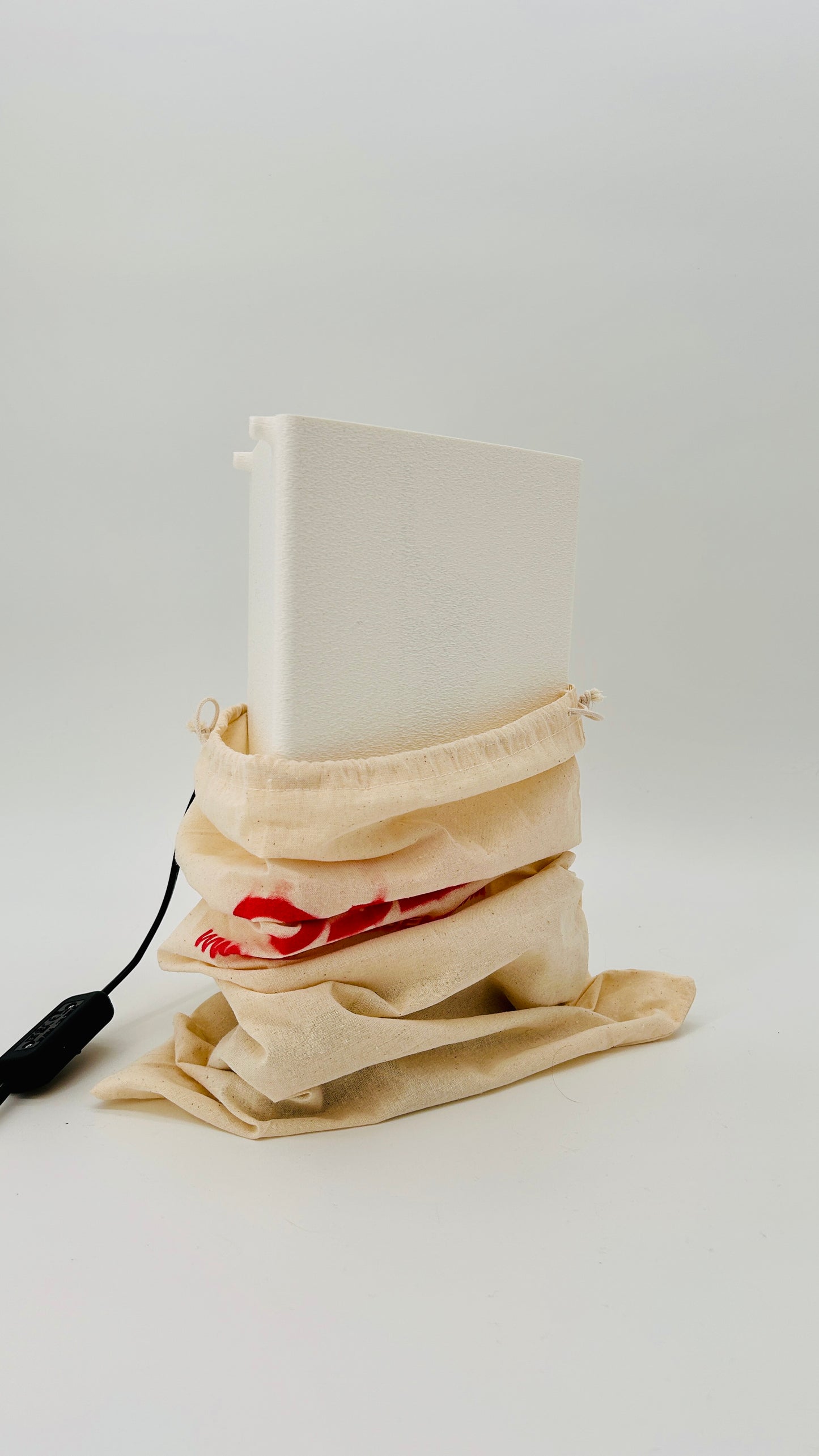 White cylindrical object in a beige drawstring bag with a red logo on a light gray background