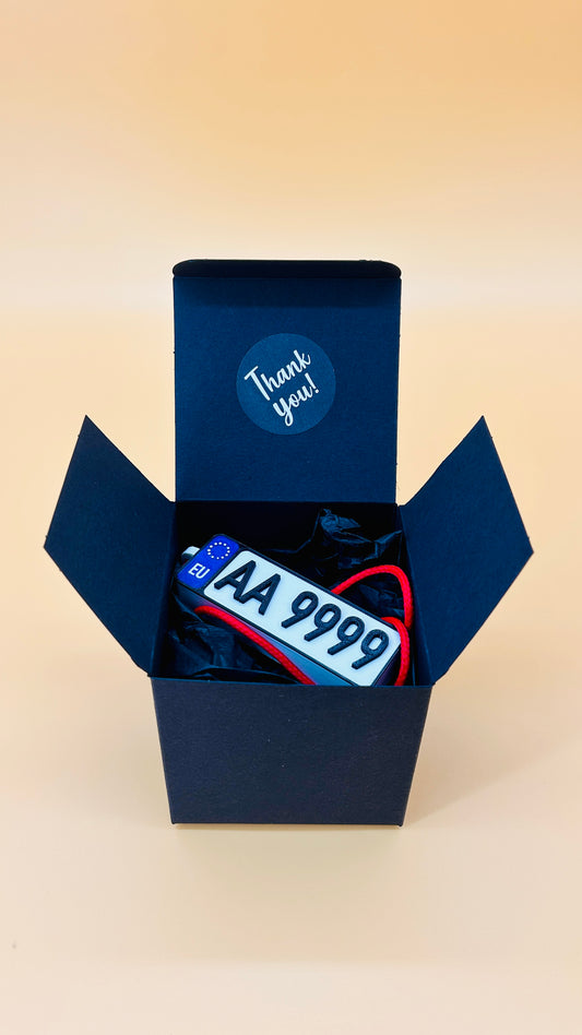 Open blue box containing a license plate and a keychain with text, on a beige background