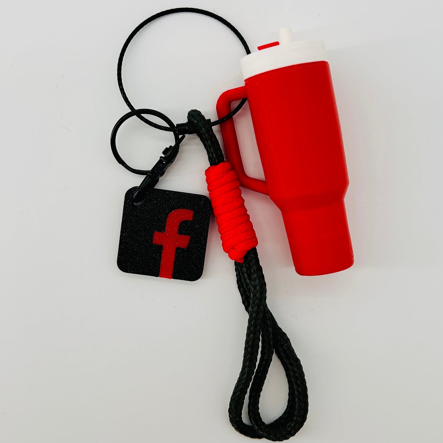 A red and white insulated coffee mug with a black handle, attached to a black braided lanyard and a black square tag featuring a red Facebook 'f' logo, shown on a plain white background.